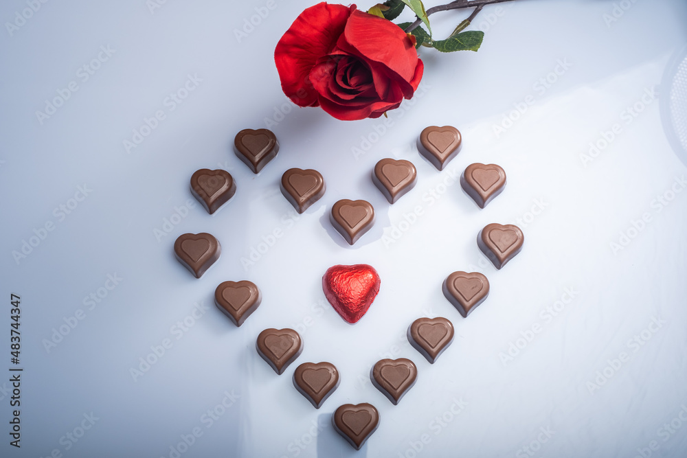 Closeup of heart shaped chocolate confections, and red roses against a bright white background.