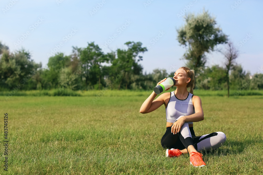 Young woman in sportswear sitting on grass and drinking protein shake Young woman in sportswear sitting on grass and drinking protein shake