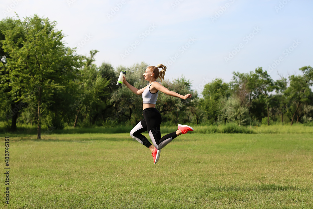Young woman jumping with bottle of protein shake in her hands outdoors Young woman jumping with bottle of protein shake in her hands outdoors