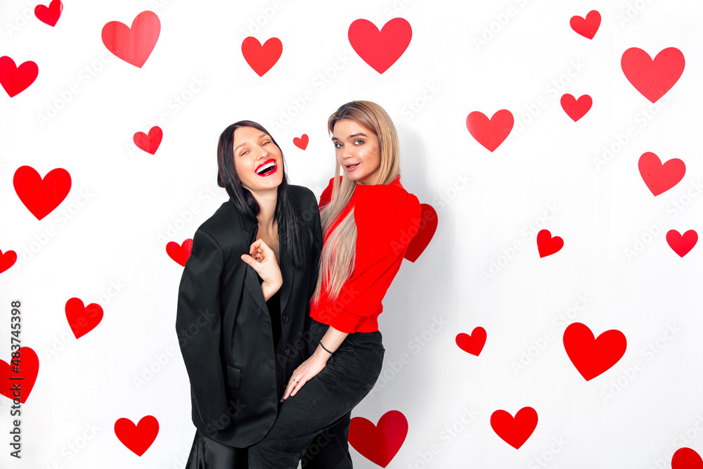 Two young adult women friends beautiful and happy together having fun with hearts on the background Two young adult women friends beautiful and happy together having fun with hearts on the background