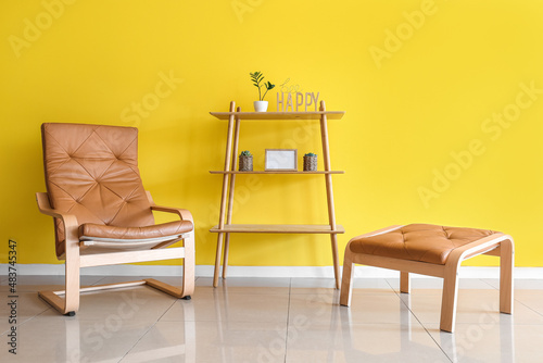 Modern armchair  ottoman and shelving unit near yellow wall