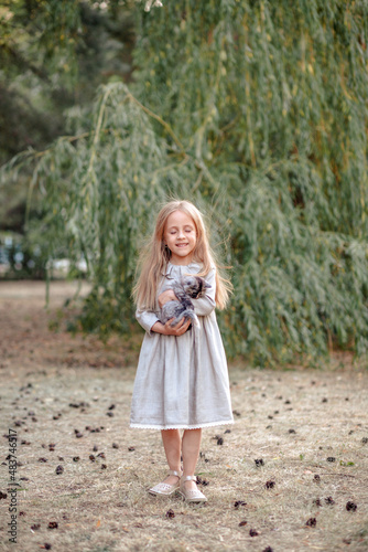 Funny little blonde girl of 7 years old in casual summer clothes posing on the street holding a kitten in her arms. The concept of a child's lifestyle.