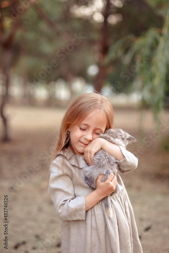 Funny little blonde girl of 7 years old in casual summer clothes posing on the street holding a kitten in her arms. The concept of a child's lifestyle.