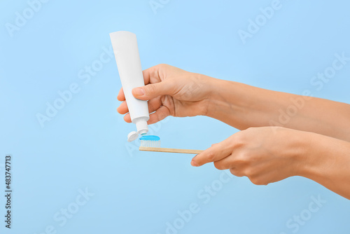 Quadro em tela Woman squeezing tooth paste onto brush on blue background