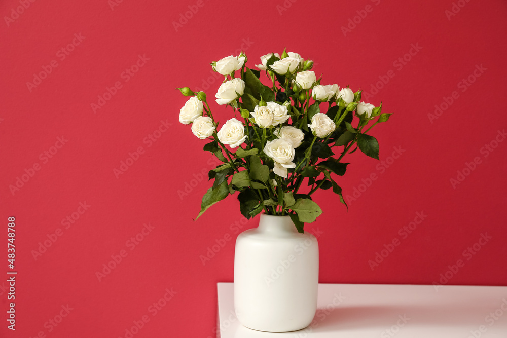 Fototapeta premium Vase with bouquet of beautiful roses on table near red wall