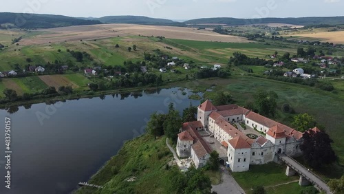 Aerial drone shot of historic castle on hill near lake, medieval architecture and cultural landmark in rural Svirzh, near Lviv Ukraine on warm sunny summer day. Tourist and travel attraction.