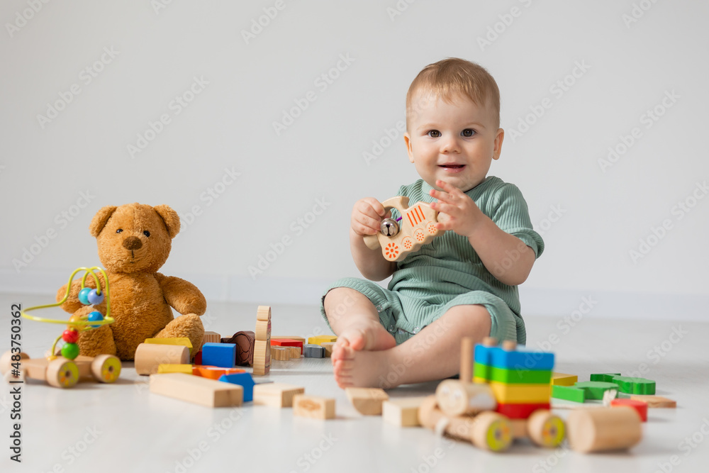 cute baby in a green cotton bodysuit is sitting on the wooden floor of the house playing educational wooden toys. products for children, early development, nursery kindergarten. space for text. cute baby in a green cotton bodysuit is sitting on the wooden floor of the house playing educational wooden toys. products for children, early development, nursery kindergarten. space for text.
