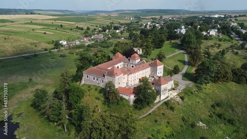 Aerial drone shot of historic castle on hill near lake, medieval architecture and cultural landmark in rural Svirzh, near Lviv Ukraine on warm sunny summer day. Tourist and travel attraction.