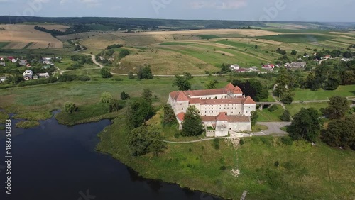 Aerial drone shot of historic castle on hill near lake, medieval architecture and cultural landmark in rural Svirzh, near Lviv Ukraine on warm sunny summer day. Tourist and travel attraction.