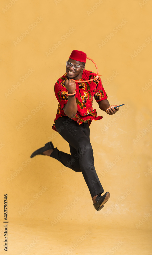Igbo Traditionally Dressed Business Man in Mid Air with Phone in Hand Celebrating