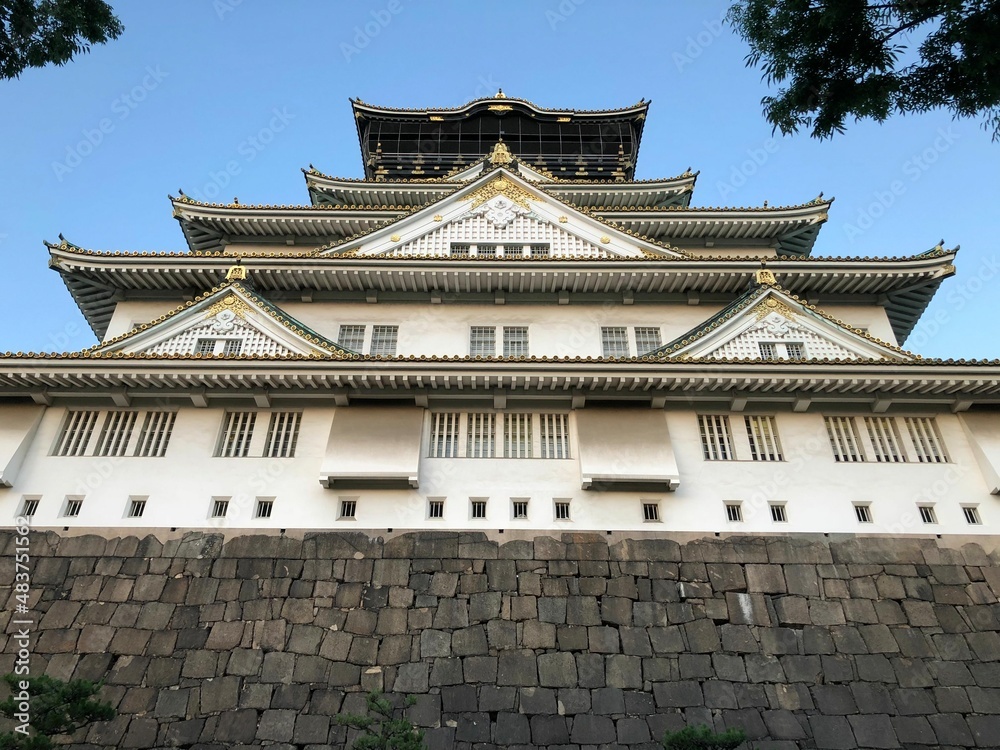 A famous historical sightseeing spot in Japan Osaka Jo castle above the stone wall in the park in summer under the blue sky taken from the low angle A famous historical sightseeing spot in Japan Osaka Jo castle above the stone wall in the park in summer under the blue sky taken from the low angle
