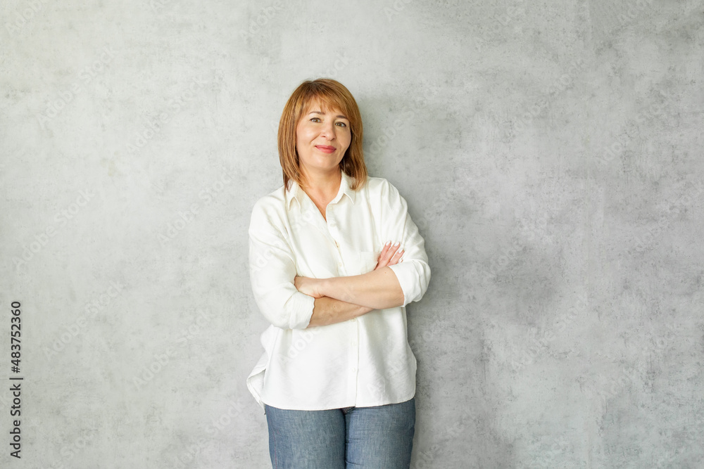 Happy mature woman with crossed arms in casual clothing standing on grey background with copy space. Happy mature woman with crossed arms in casual clothing standing on grey background with copy space.