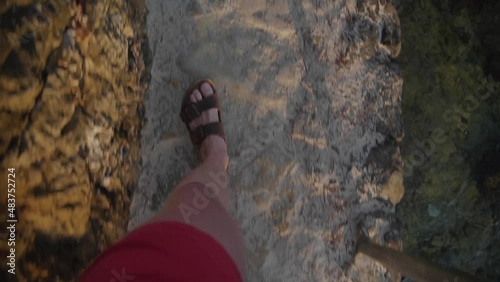POV of young male walking a stone path in sandals on the rocky coastline of Mallorca during vacation at the ocean in the morning
 photo