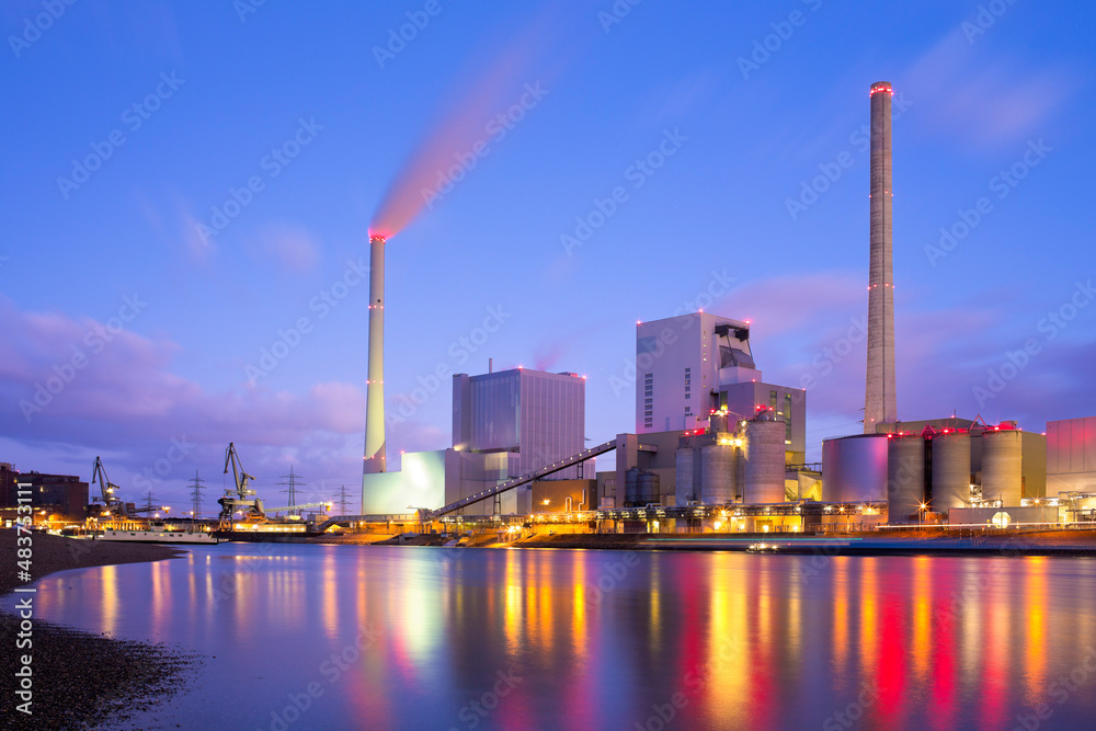 Large illuminated coal power plant with reflected lights in the water of a river