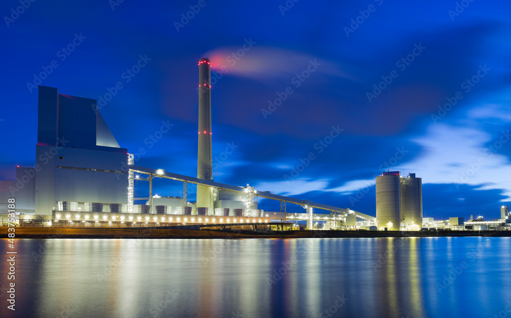 Large illuminated coal power plant with reflected lights in the water of a river