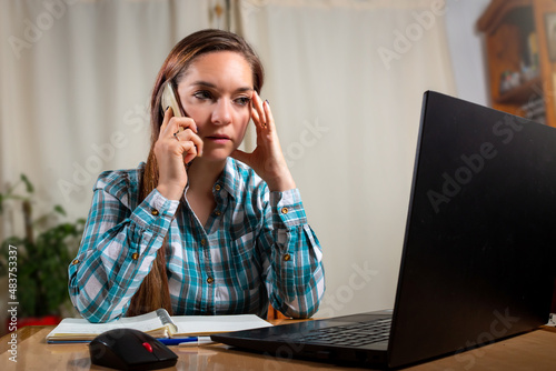 Mujer preocupada hablando por telefno mientras trabaja con su laptop photo