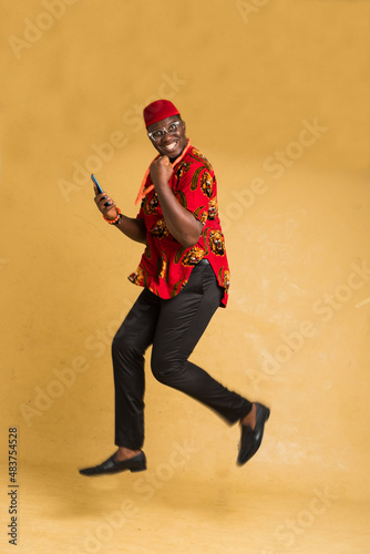 Igbo Traditionally Dressed Business Man in Mid Air with Phone in Hand Side View photo