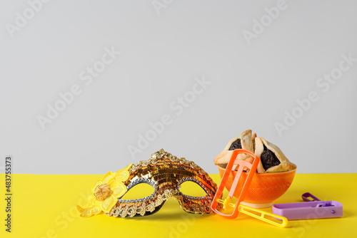Bowl with hamantaschen and decor for Purim holiday on table against grey background