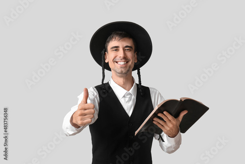 Hasidic Jewish man with Torah showing thumb-up on light background