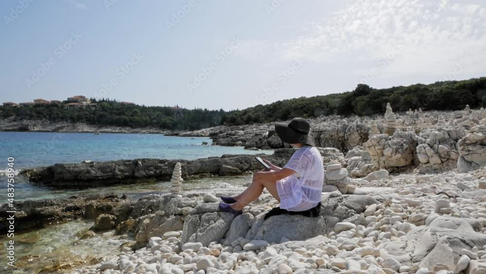 Girl Using Mobile Phone While Sitting On The Rocky Shore Of Emplisi Beach In Greece. - static Girl Using Mobile Phone While Sitting On The Rocky Shore Of Emplisi Beach In Greece. - static
