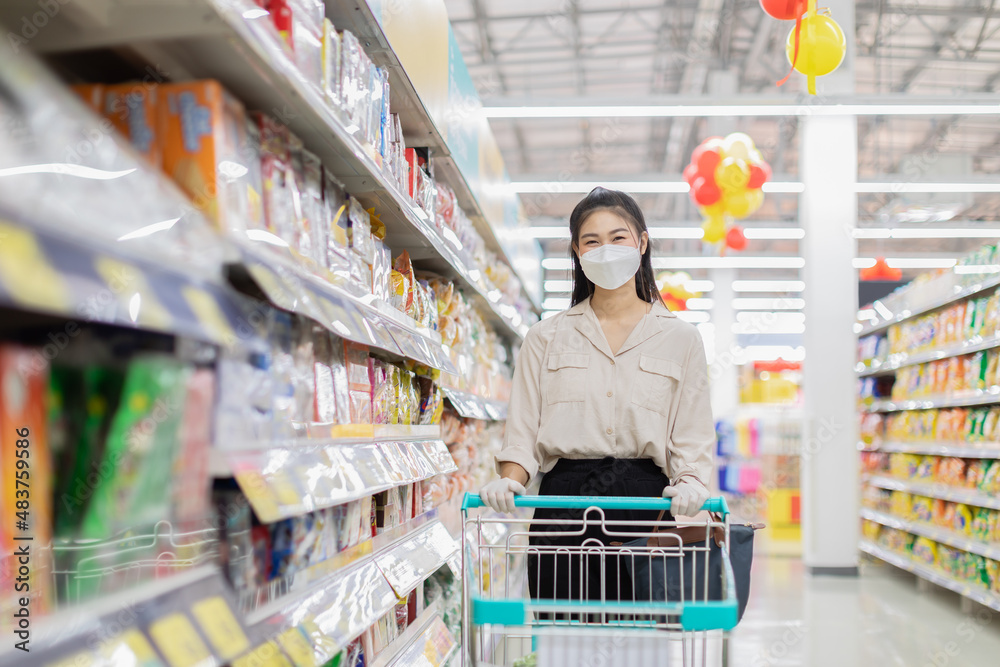 Beautiful attractive asian woman wearing medical face mask and rubber gloves for protected virus and bacteria smile with shopping cart in supermarket happiness and enjoy,Shopping in Grocery Concept