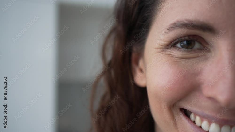 Young woman with long curly brunette hair smiles broadly and blinks looking into camera lens happily crop half face extreme closeup