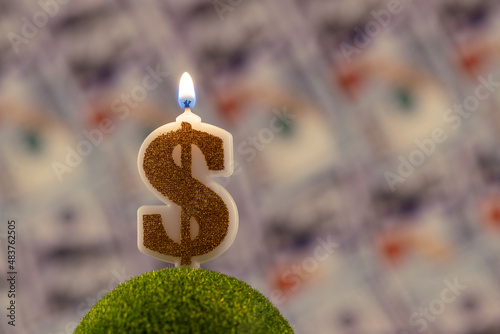 A burning candle in the form of an American dollar symbol on the background of 100 American dollars bills photo