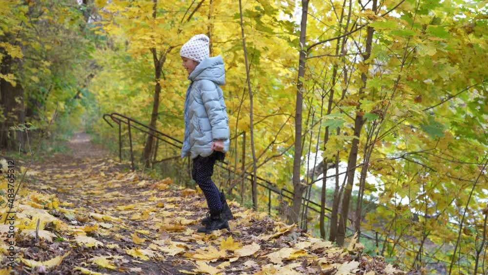Little girl turns in front of camera, standing on blurry autumn background. Smiling girl spinning in the park looks at the camera. Handsome kid stylish urban young lifestyle outside person Little girl turns in front of camera, standing on blurry autumn background. Smiling girl spinning in the park looks at the camera. Handsome kid stylish urban young lifestyle outside person