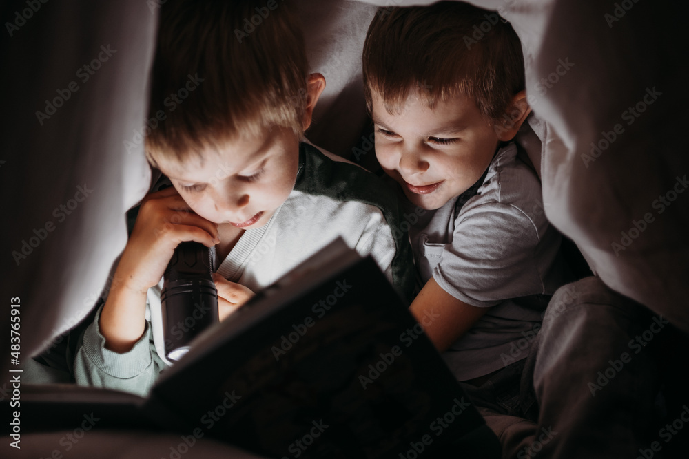 Two little brothers reading a book at night hiding under the blanket Two little brothers reading a book at night hiding under the blanket