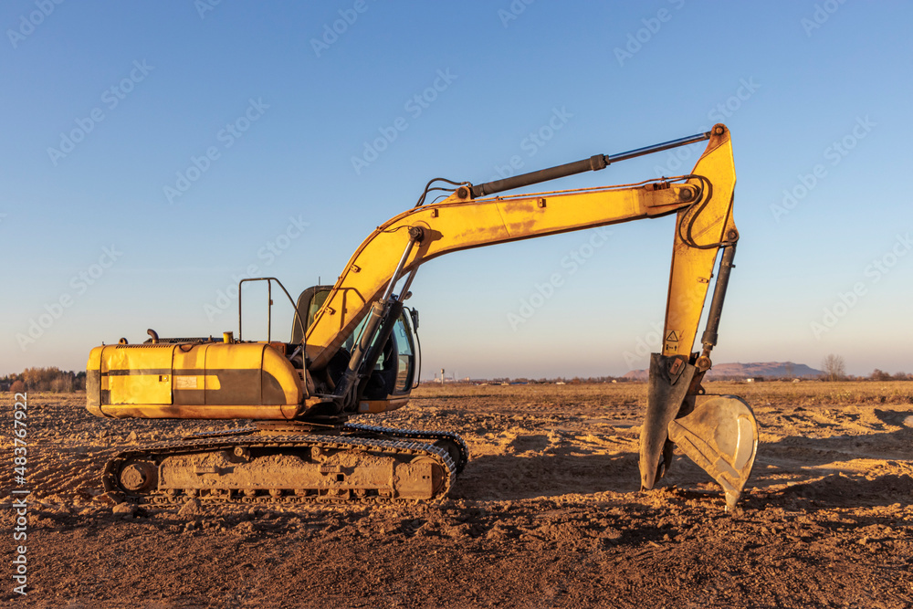 Backlit excavator on an industrial site against the background of the evening sky. Construction machinery for earthworks. Backlit excavator on an industrial site against the background of the evening sky. Construction machinery for earthworks.