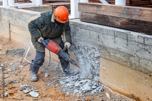 Bild auf Leinwand A worker with a jackhammer at a construction site levels a concrete wall