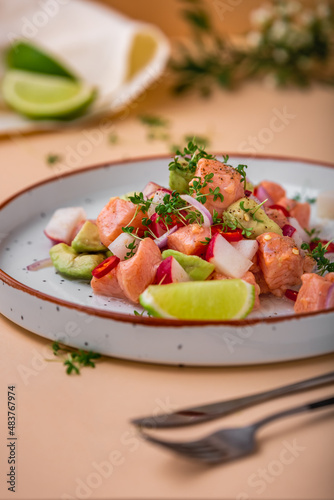 Salmon ceviche with avocado, onion, radish and lime on white plate and on beige background. Peruvian food. Delicious ceviche with salmon.
