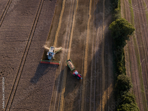 Woodbridge Suffolk UK August 12 2021: Aerial shot of combine loading off corn grains into tractor trailer. Farming concept, harvesting concept