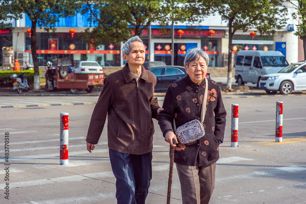 ANQING, CHINA - MARCH 21: Senior Man and Woman walk crossing Street. A senior couple, 80 years old, helping each other, walk crossing the street on March 21, 2014