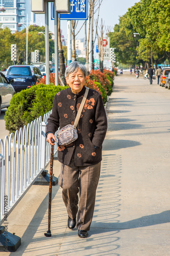 ANQING, CHINA - MARCH 21: Senior woman walks on street. A 80 years old Chinese lady with a cane walks on the street on March 21, 2014..