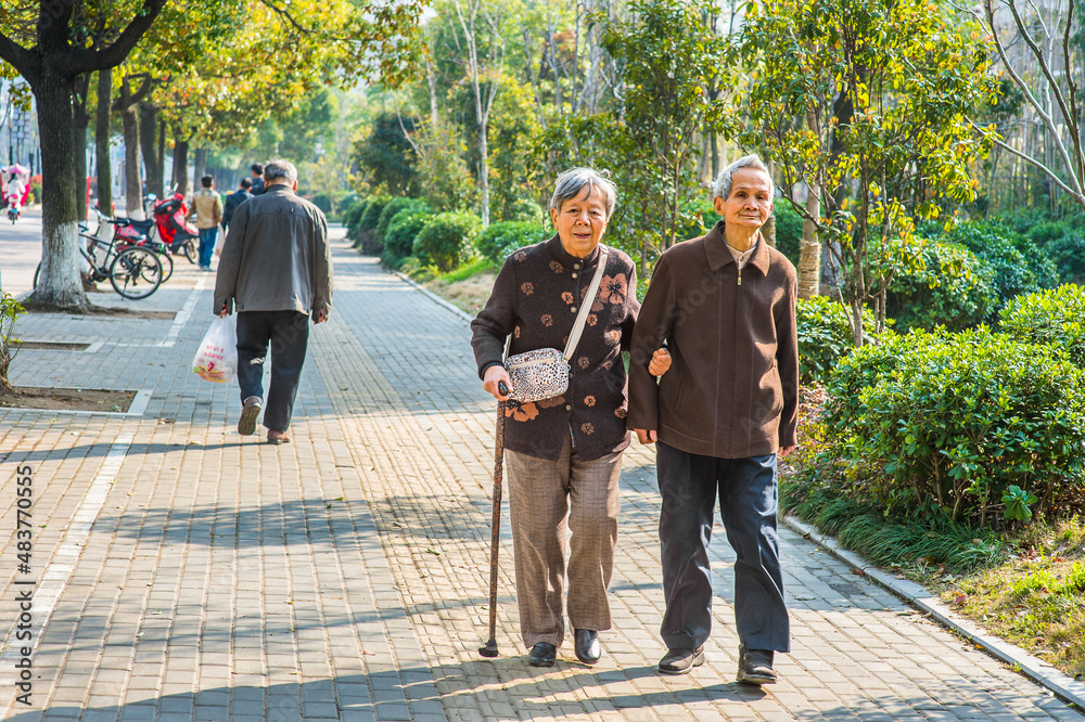 Senior Man and Woman Walking Outside. A senior couple, 80 years old, helping each other, is walking on street, woman holding a walking stick..