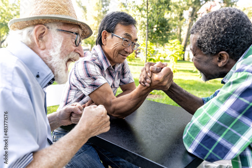 Group of senior friends playing arm wrestling at the park. Old multiethnic friends making activities outdoor. Concept about third age and lifestyle