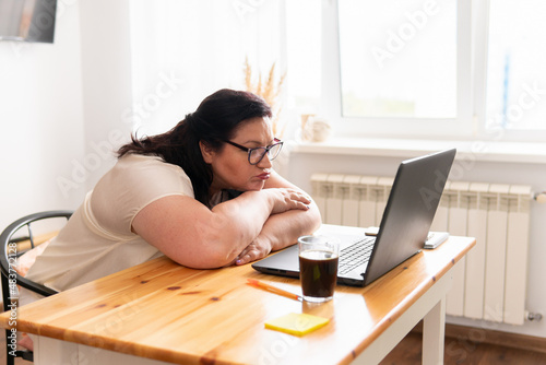 A woman is sitting in a room at a table with a laptop.
