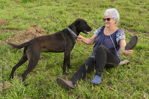 Elderly happy woman playing with her pet on the lawn.Black dog.