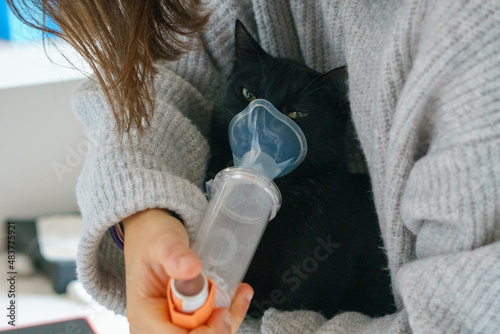 A black cat taking its daily dose of a cough curative medicine. A young woman giving her cat its care daily dosis. Owner giving the inhaler to her little kitten
 photo