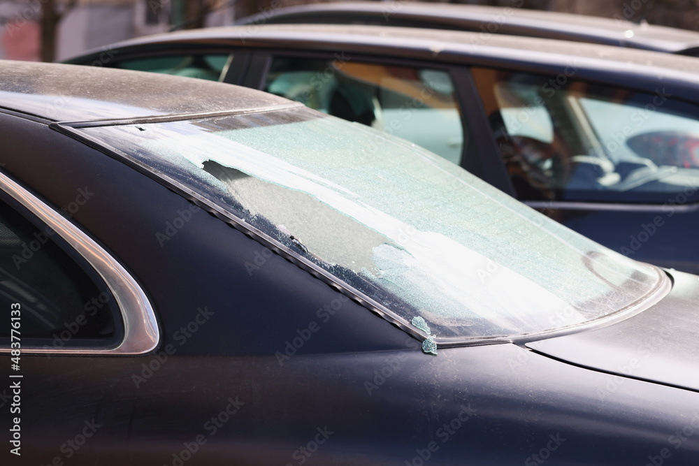 Broken rear window of a black car on the street, close-up