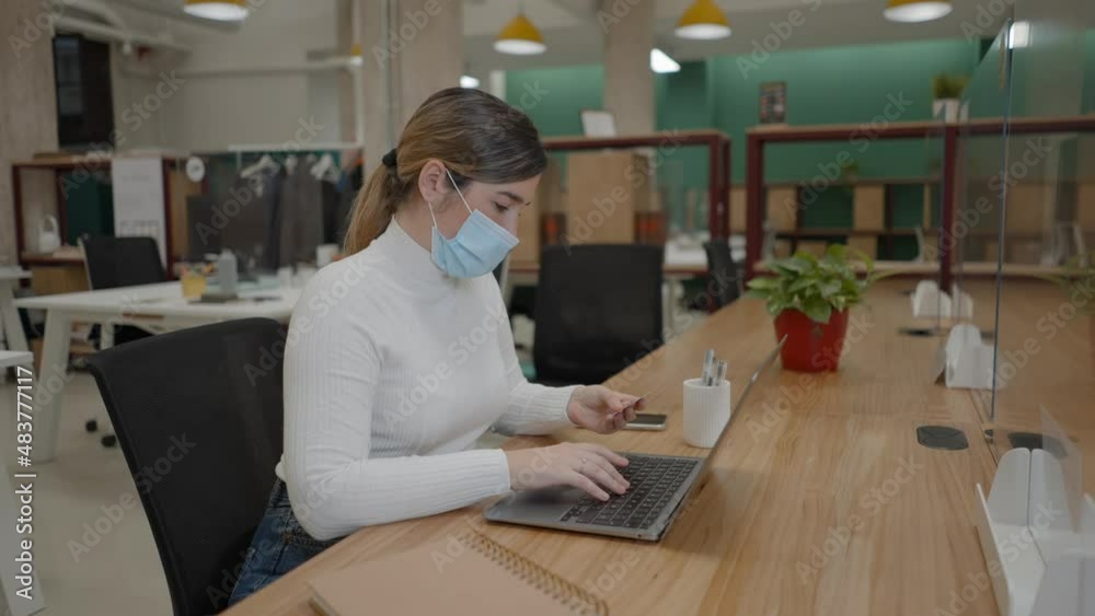 Woman in protective face mask using credit card for online payment with laptop in coworking office Woman in protective face mask using credit card for online payment with laptop in coworking office