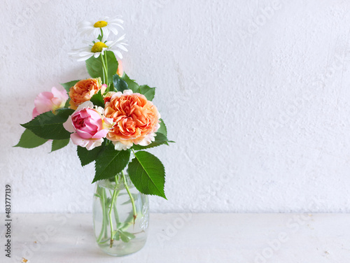 Spring flowers in a glass vase on a wooden table. Blurred kitchen background. Bouquet of roses and Leucanthemum. Contemporary elegant scandi interior.