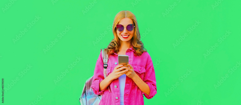 Portrait of stylish happy smiling young woman with smartphone wearing pink jacket, sunglasses on green background Portrait of stylish happy smiling young woman with smartphone wearing pink jacket, sunglasses on green background
