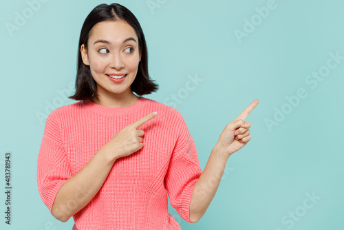 Young smiling happy woman of Asian ethnicity 20s wear pink sweater point index finger aside on workspace area mock up isolated on pastel plain light blue background studio People lifestyle concept.