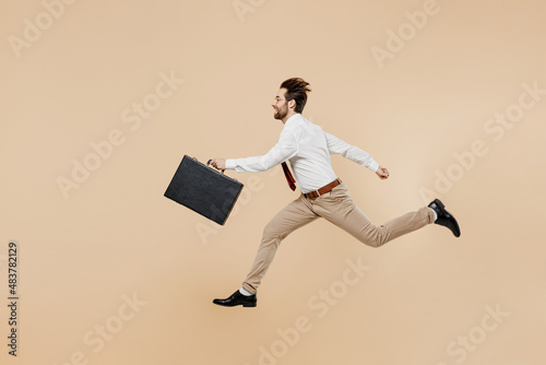 Full body side view young employee business man corporate lawyer 20s wear white shirt red tie glasses work in office jump run fast hold briefcase isolated on plain beige background studio portrait photo