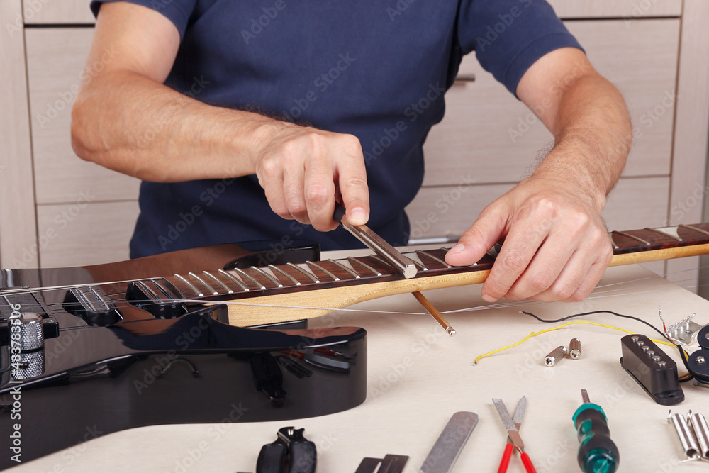 Fototapeta premium Guitar technician crowning frets on guitar neck with fret files.