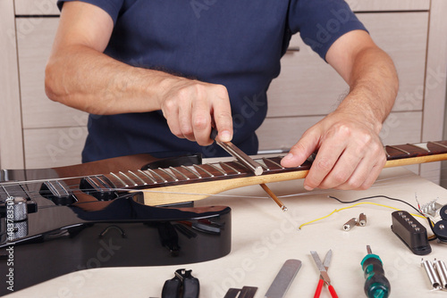 Guitar technician crowning frets on guitar neck with fret files.
