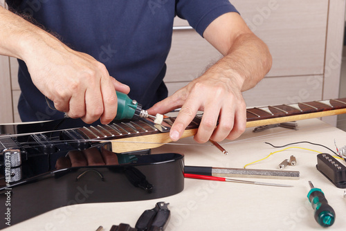 Guitar technician polishes frets on guitar neck with polishing machine.