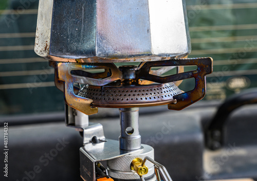 close-up of the burner of a camping gas stove, lit against which the bottom of a small Italian coffee pot can be seen